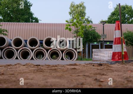 Large concrete rings are stacked on top of each other. Smaller ones are placed inside bigger ones. A red and white cone nearby warns about constructio Stock Photo