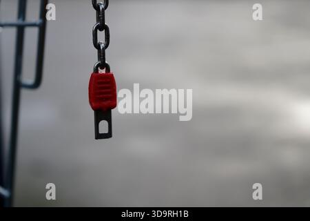 A red key attached to a chain is inserted into the lock mechanism of a metal shopping cart. Part of the metallic cart is also visible in the image. Stock Photo