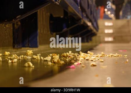 Blue seats are lifted revealing scattered popcorn and trash on the floor beneath in a movie theater with steps visible in the background. Stock Photo