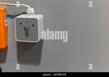 White key controlled electrical switch mounted on gray wall requiring key insertion to turn right for on position left for off with neutral middle set Stock Photo