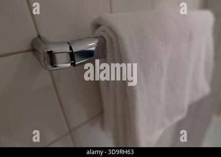 A white towel rack is mounted on the wall of a bathroom. It stands against a background of white tiles. One of the joints appears slightly broken, sho Stock Photo