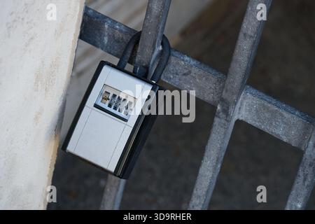 A black and white combination lock with numbered dials is securely attached to a metal fence, designed for access control using a personal pin code. Stock Photo
