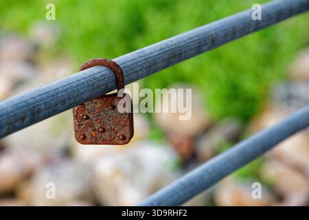 A deeply rusted padlock hangs on a metal structure, likely placed long ago by a couple as a love lock. Its flaking rust shows time passage since the k Stock Photo