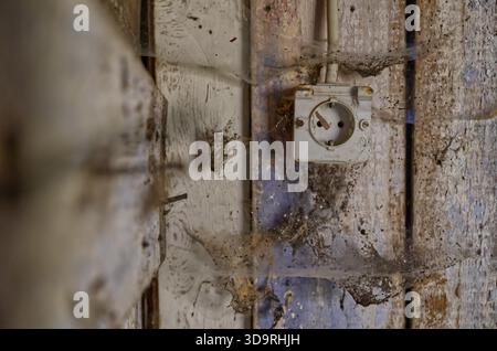 A worn wooden wall covered in thick layers of dust, cobwebs, and dirt. A small white plastic outlet is mounted on the wall, contrasting with the aged Stock Photo