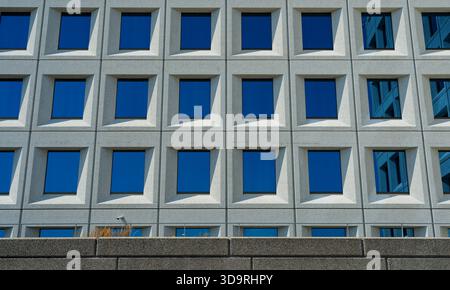A long granite building features numerous identical reflective windows that mirror the surroundings perfectly. The sleek, polished glass creates a mes Stock Photo
