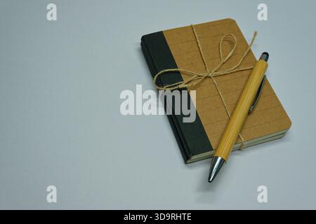 Two eco friendly notebooks made from natural brown paper are neatly tied together with a rustic fiber ribbon in a bow.A wooden style pen rests on top, Stock Photo