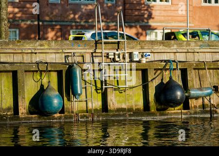 A close up view shows four marine fenders two round and two elongated hanging from ropes along the edge of a harbor pier to prevent damage to vessels Stock Photo