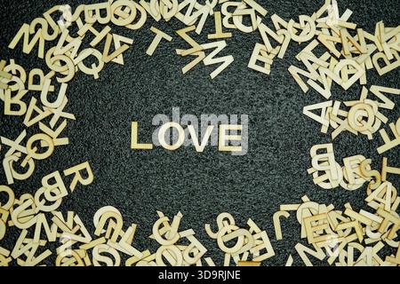 The word love is spelled out with wooden letters in the center of a black rubber mat while various other wooden letters are scattered around, creating Stock Photo