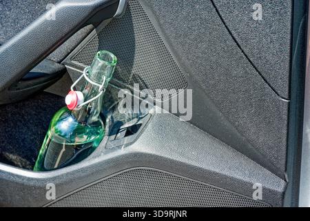 A car door compartment holds a glass bottle with with water and a metal swing top cap. The bottle appears to be from Flensburger beer but contains cle Stock Photo