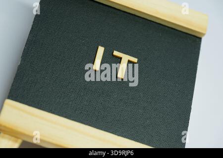 Simple wooden letters forming the word IT are placed on a black fabric background. A symbolic and stylish visual linked to digital, software, or tech Stock Photo
