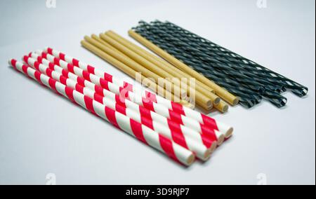 Three different drinking straws shown on a white background. Includes red and white striped paper straws, golden eco friendly paper straws, and green Stock Photo
