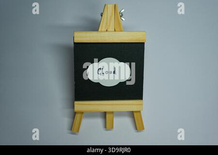 A wooden stand holds a small black fabric screen with a paper cloud pinned to it. The cloud has the word CLOUD written on it with marker, symbolizing Stock Photo