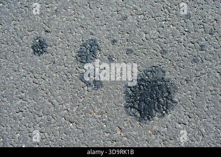 An asphalt surface shows visible stains from spilled oil or diesel, creating patterns that reflect environmental pollution and contamination on urban Stock Photo