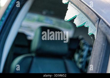 A purple car passenger side window is shattered, with glass shards both inside and outside the frame. The sharp fragments stick out from the broken ed Stock Photo