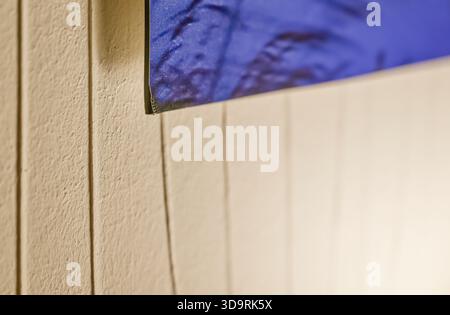A beige wall with vertical stripes holds a blue fabric piece hanging loosely. The material resembles bedding, adding a casual and domestic touch to th Stock Photo