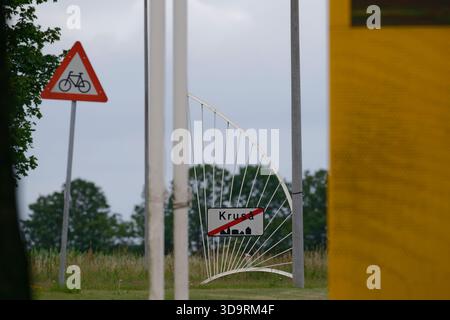 A metal pole supports a curved decorative bracket holding a town sign. The word Krusa in Denmark is crossed out, indicating the town��s end, with a red Stock Photo