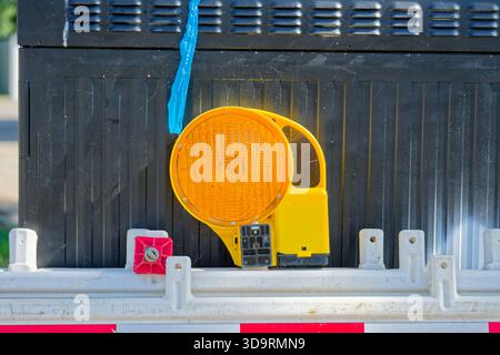 Several plastic barriers lean together in storage before deployment. White panels with red bands and amber reflectors rest on pavement, ready to close Stock Photo