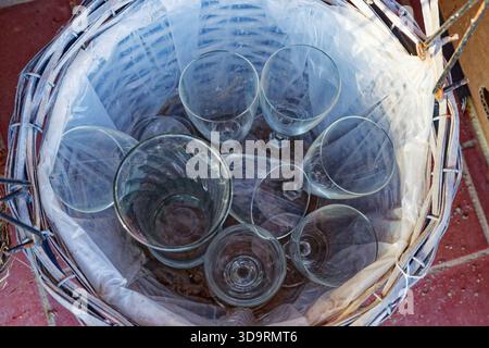 A lined basket holds a clear bag filled with drinking glasses and cups. Some glass is broken into small shards, yet the pieces still look tidy in the Stock Photo