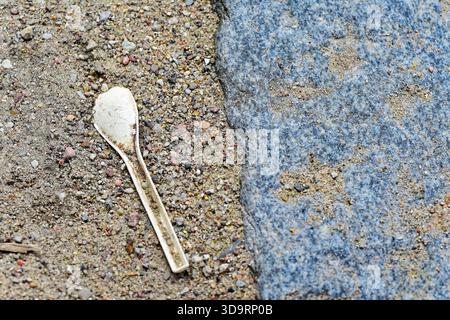 A small paper spoon rests on pale gravel beside a large natural stone. Minimal outdoor scene ideal for ecology messages, cleanup campaigns, background Stock Photo