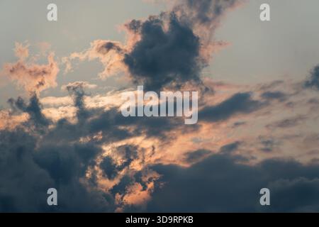 Layered gray clouds drift across the sky while warm pink light spills from the sun behind them. Atmospheric sunset backdrop perfect for posters, web h Stock Photo