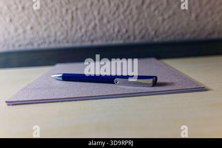 Several sheets of paper rest on a wooden table while a blue plastic pen with a shiny silver tip lies across the pages and soft daylight gives a clean Stock Photo