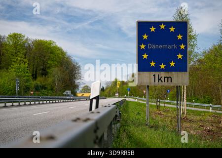 A second view frames the tall blue plaque with golden stars marking the Denmark frontier in Flensburg while cars stream past the guardrail. The board Stock Photo