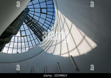 A clear dome spans above a white wall, its metal framework forms a fine grid and the sun casts patterned shadows across the surface, light and structu Stock Photo