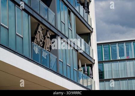 A modern residence shows full glass fronts and wide balconies, railings shine, on the terraces the sun umbrellas are tied and waiting, the structure f Stock Photo