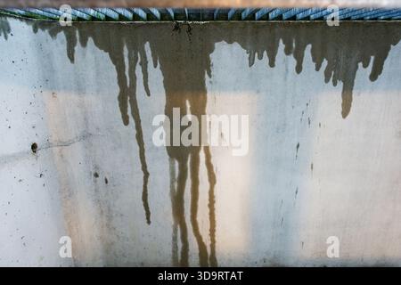 A plain concrete wall shows dark wet streaks suggesting water leaking from above the surface is rough and stained the pattern of moisture reveals line Stock Photo