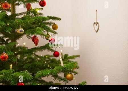 A beautifully decorated Christmas tree with red and gold ornaments, candles, and twinkling lights. A heart-shaped ornament hangs on the wall nearby, a Stock Photo