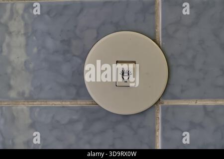 A close-up of a light switch on a tiled wall. The switch features a symbol resembling a light bulb or flame, indicating its function. The tiles are a Stock Photo