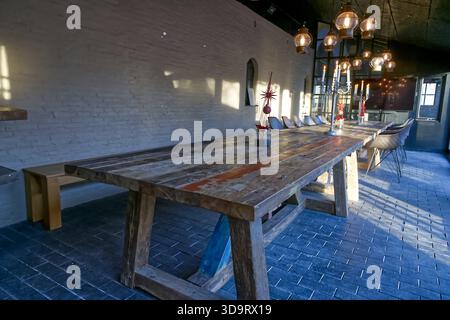 A spacious nordic dining area featuring a large rustic wooden table with a unique design, surrounded by modern chairs. The room is illuminated by pend Stock Photo