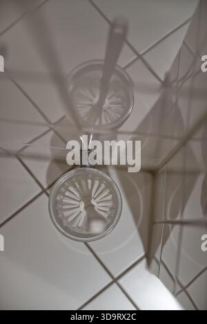 A top view of a toilet brush holder on a tiled floor, showing the brush and its reflection on the tiles in a bright bathroom with light tiles. Stock Photo