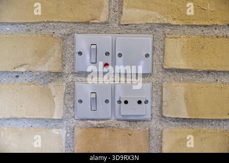A close-up view of old danish electrical switches and a socket mounted on a textured brick wall. The switches include a toggle switch and a push butto Stock Photo