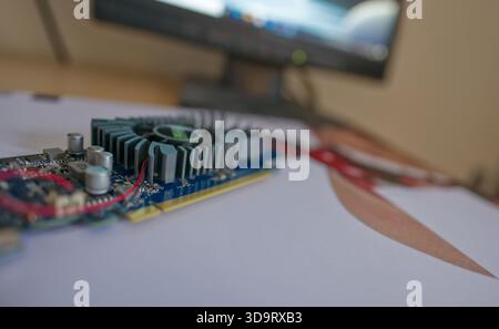 A close-up of a computer graphics card placed on a printed sheet, with a blurred monitor in the background. The image showcases the intricate details Stock Photo