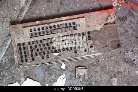 A dusty, old computer keyboard lying on a dirty surface, with a connector piece nearby. The keyboard shows signs of wear and neglect, surrounded by de Stock Photo