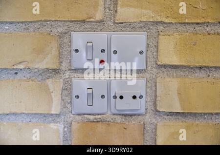 A close-up view of electrical switches and a socket mounted on a textured brick wall. The switches include a toggle switch and a push button, with a r Stock Photo