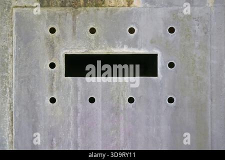 A close-up view of a textured concrete wall featuring a rectangular opening surrounded by several circular holes. The surface shows signs of weatherin Stock Photo