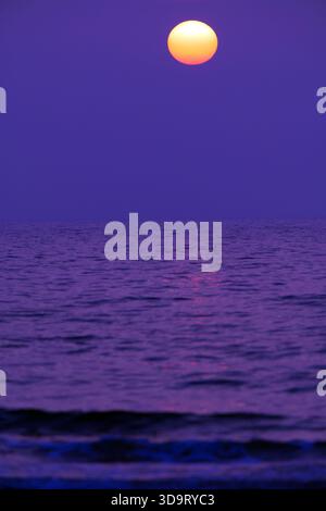 A serene Pink and Blue sunset over the ocean, with a large orange sun setting against a purple sky. The water reflects the warm colors, creating a tra Stock Photo