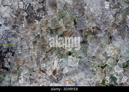 A close-up view of crushed ice with some green grass peeking through. The ice pieces are irregularly shaped and glisten in the light, creating a textu Stock Photo
