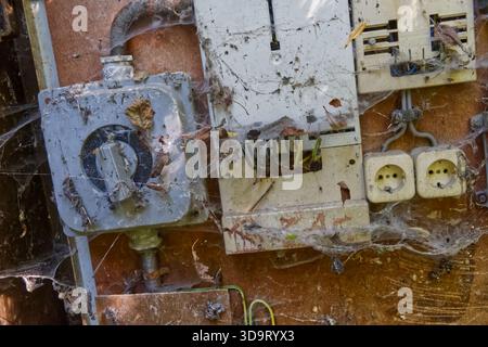 An old, dusty electrical panel covered in cobwebs and debris, showcasing neglected wiring and outlets. The panel is mounted on a weathered wooden surf Stock Photo