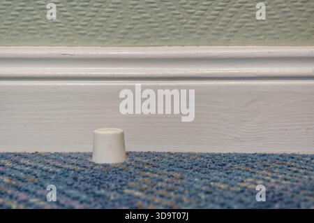 A close-up view of a small white plastic cap resting on a blue carpet, with a textured green wall and white baseboard in the background. Stock Photo
