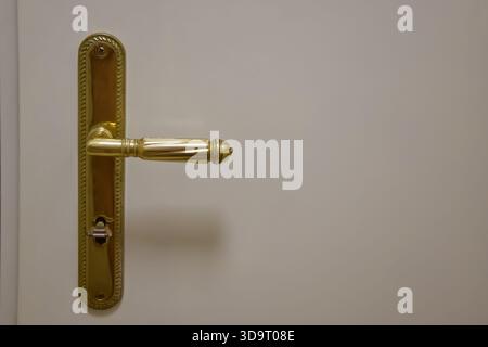 A close-up view of a vintage gold door handle on a white door. The handle features intricate detailing and a classic design, adding elegance to the do Stock Photo