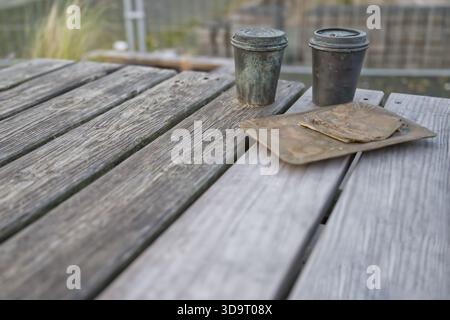 A rustic wooden table with two old containers and a metal plate with a circular object on it. The scene has a natural outdoor setting, with greenery i Stock Photo