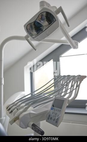 A dental chair setup featuring an overhead light and various dental instruments. The scene is well-lit with natural light coming through a window, cre Stock Photo
