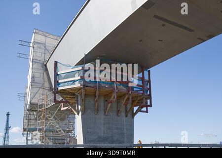A close-up view of a bridge under construction, showcasing the concrete support structure and scaffolding. The sky is clear with a few clouds, highlig Stock Photo