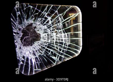 A close-up view of a shattered glass pane with intricate cracks radiating from a central point, set against a dark background. Stock Photo