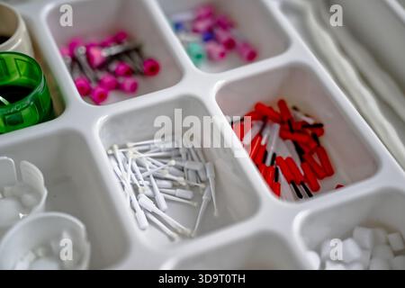A close-up view of a compartmentalized organizer filled with various small items including white and red connectors, colorful pins, and other assorted Stock Photo