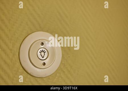 A close-up of a light switch on a textured yellow wall. The switch features a light bulb symbol, indicating its function. The design is simple and fun Stock Photo