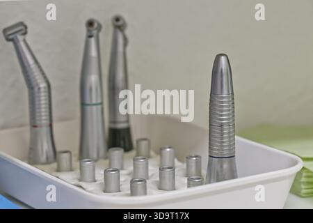 A tray containing various dental instruments, including dental handpieces and attachments, arranged neatly on a white cloth. The background is softly Stock Photo